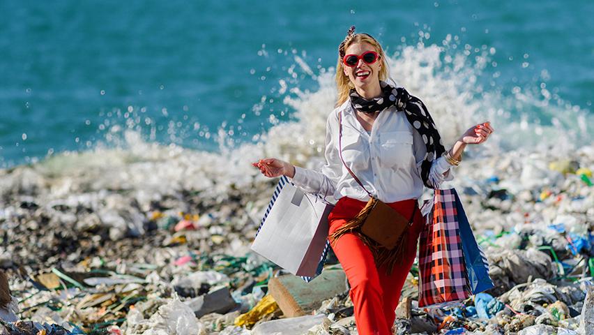 Woman standing on pile of  trash holding shopping bags at beach